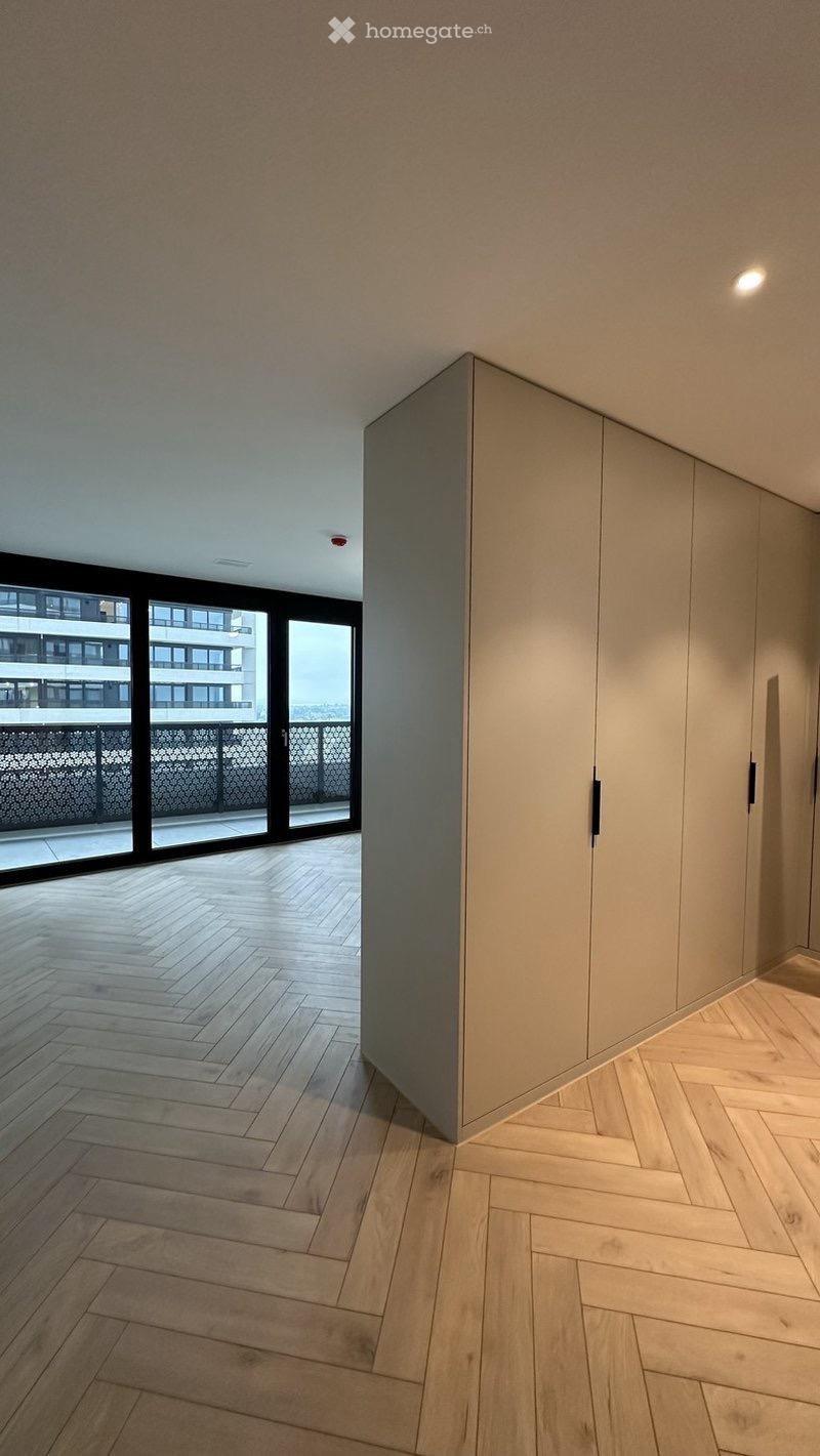 Empty room with wooden flooring, large windows, and a balcony view of a building.