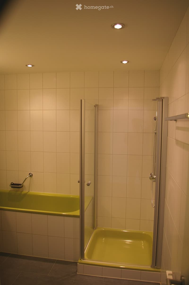 Modern bathroom with a green bathtub, glass-enclosed shower, and multiple ceiling lights.
