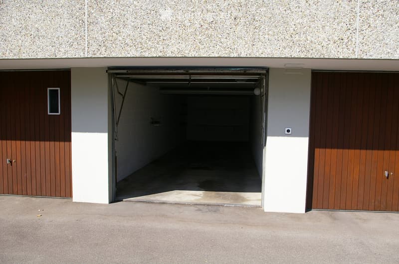 A modern garage with a textured concrete roof, two wooden garage doors, and a concrete driveway.