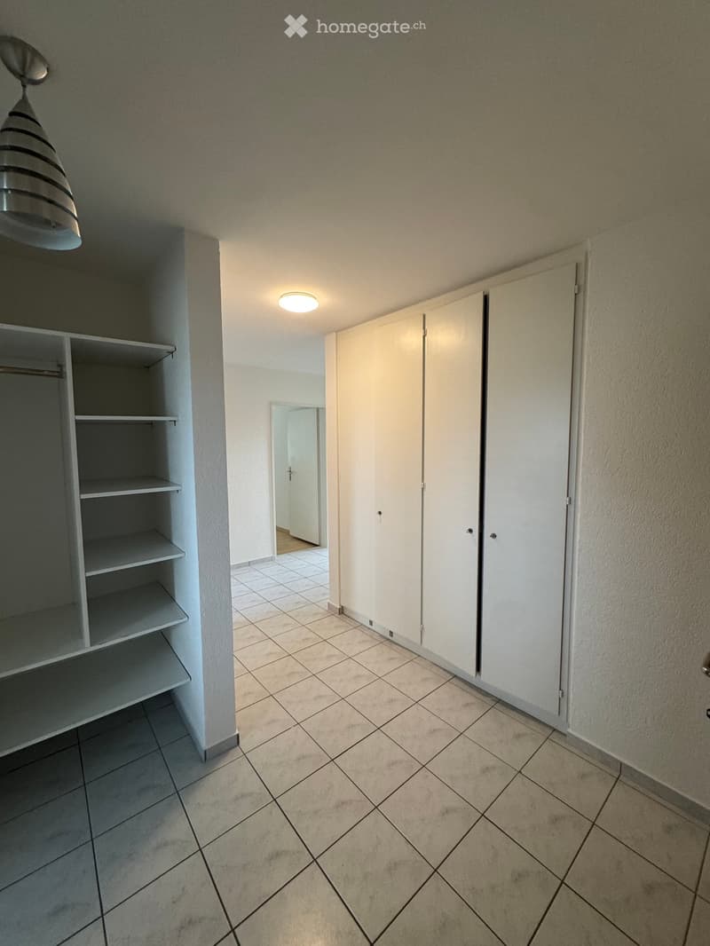 Empty room with tiled floor, white walls, built-in closet with shelves, and a doorway leading to another room.
