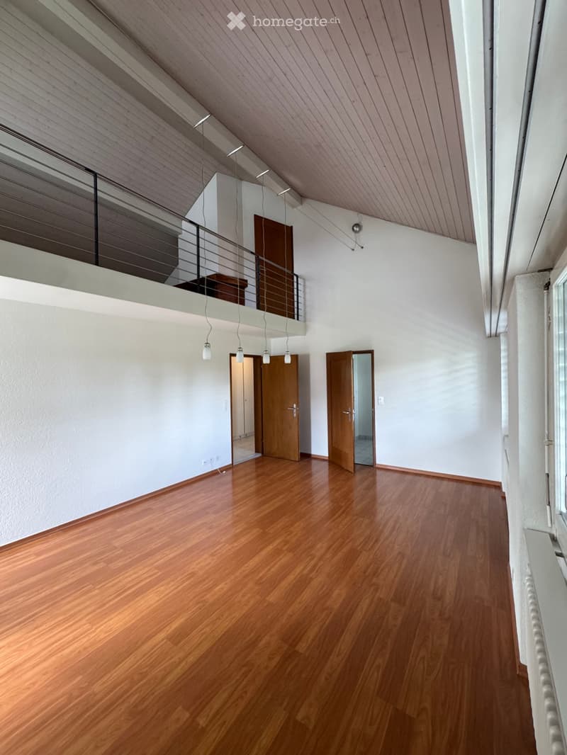 Empty room with wooden flooring, white walls, and a raised ceiling with exposed beams. Features include a metal railing leading to an upper level and several doors leading to other rooms.