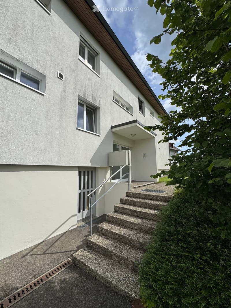 Two-story house with white exterior, multiple windows, and a small staircase leading to the entrance.