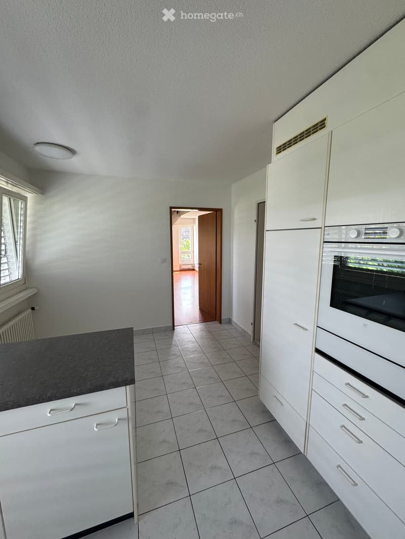 Modern kitchen with white cabinets, tiled floor, and a black countertop. An open doorway leads to another room.