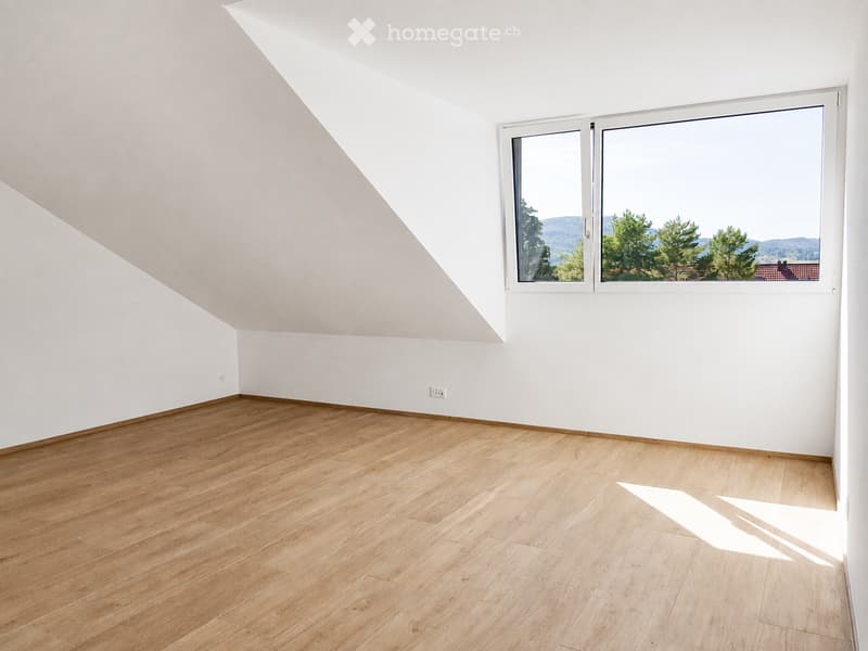 Empty room with wooden flooring and white walls, featuring a large window offering a scenic view of trees and hills.
