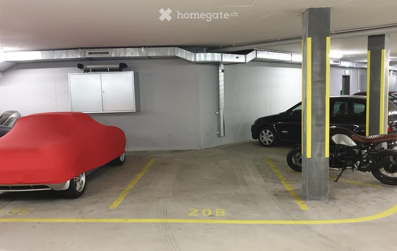Underground parking area with marked parking spaces, a covered car, a motorcycle, and a storage cabinet.
