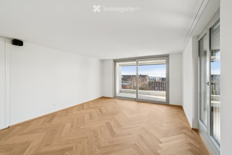 Empty room with white walls, herringbone wooden flooring, and large sliding glass doors leading to a balcony.