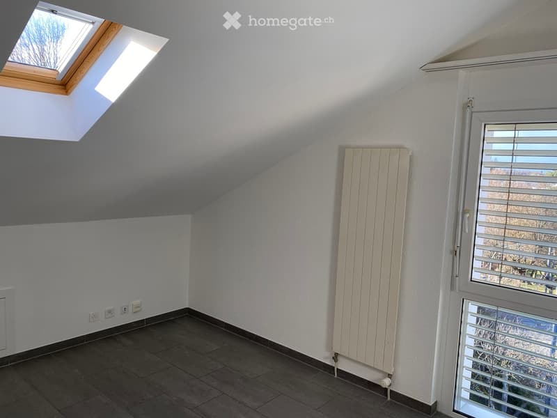 Empty attic room with slanted ceilings, skylight windows, radiator, and tiled floor.