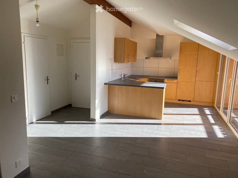 Empty room with tiled floor, white walls, and a doorway leading to a kitchen area with wooden cabinets and a countertop.