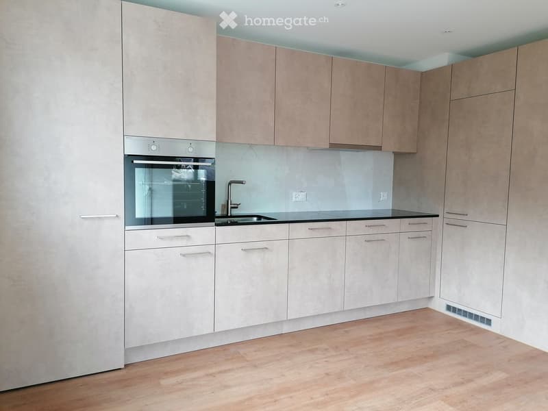 Modern kitchen with light-colored cabinets, stainless steel oven, and a black countertop.