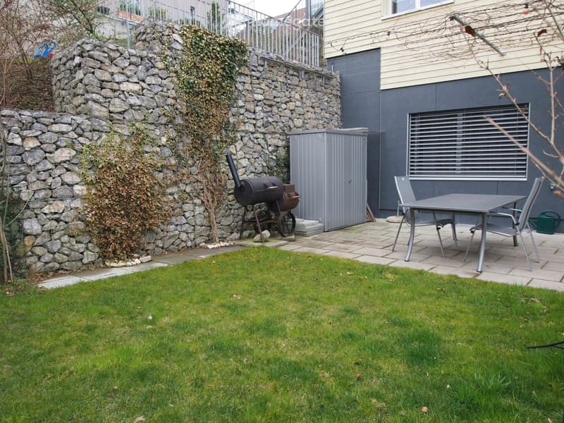 Garden with a grassy lawn, stone wall, barbecue, patio furniture, and a storage shed.