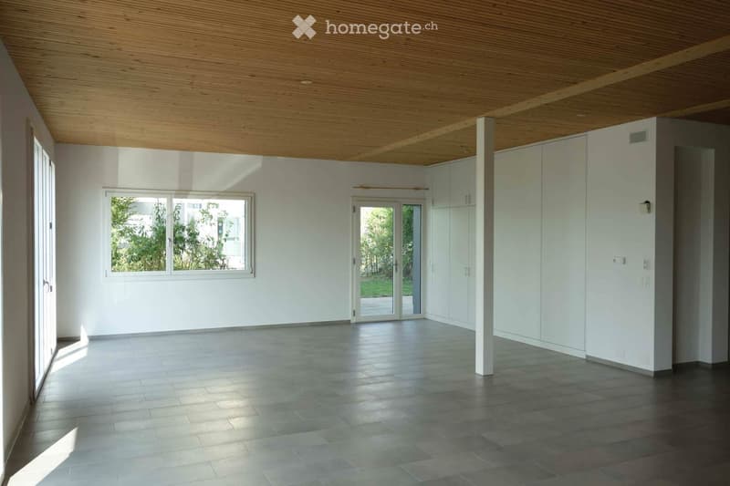 Empty room with white walls, wooden ceiling, tiled floor, large windows, and built-in white cabinets.