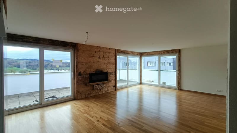 Bright, open living space with wooden flooring, large glass sliding doors leading to a balcony, and a built-in TV on a wooden wall.