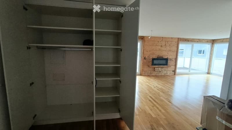 Empty room with wooden flooring, large windows, and a built-in fireplace. The closet is open, showing empty shelves and hanging space.