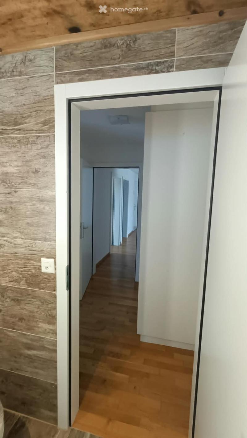 Modern hallway with wooden flooring, white walls, and a partially open door leading to another room.