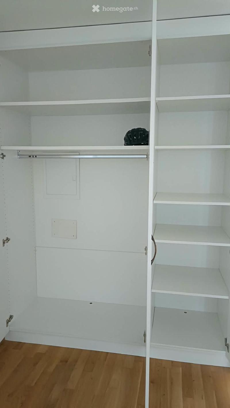 Empty closet with white shelves and a hanging rod, wooden floor visible.