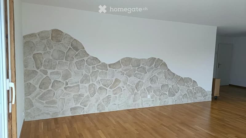 Empty room with wooden flooring and a stone-patterned wall design. No furniture or equipment present.