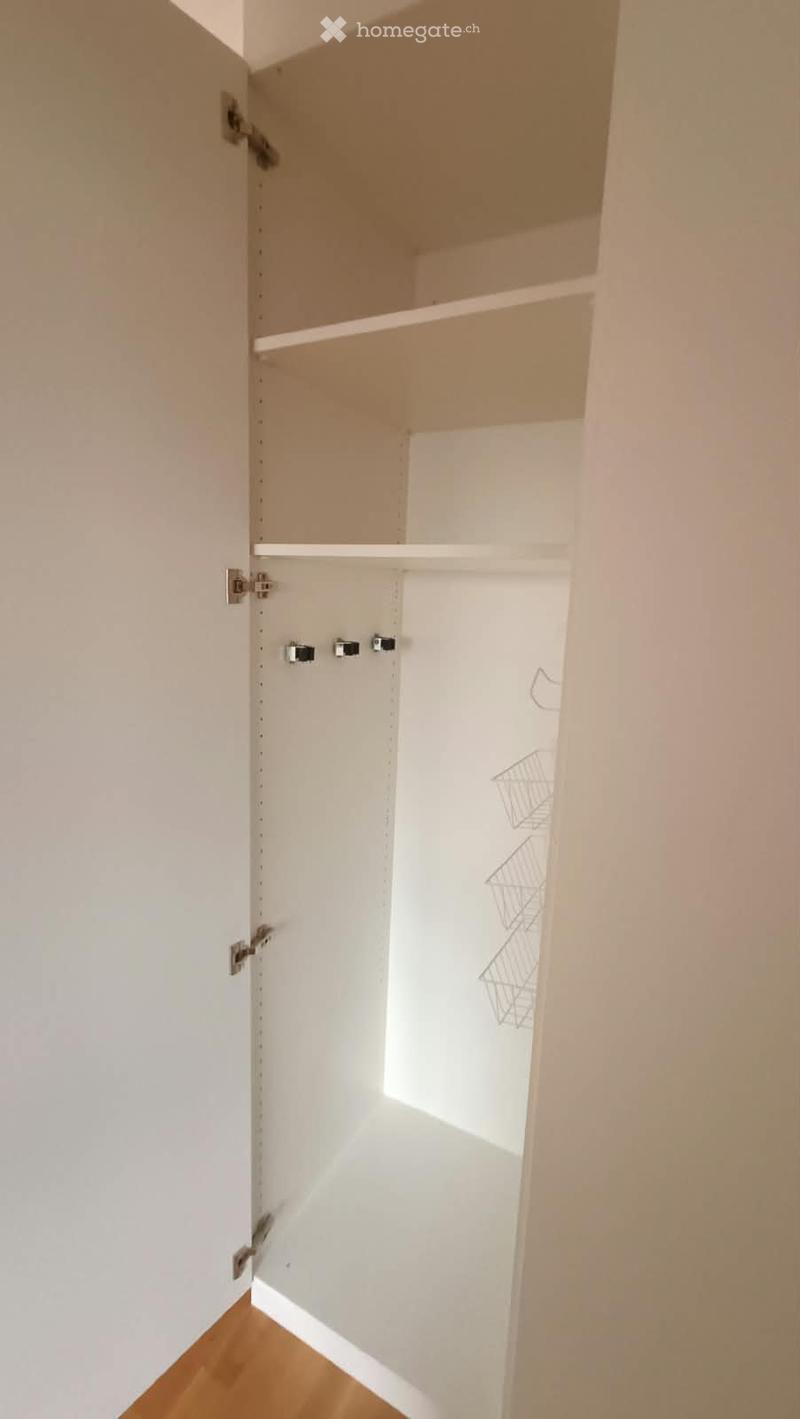 Empty closet with white walls, wooden floor, and open doors revealing empty shelves.