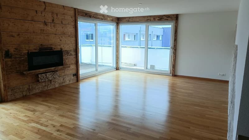 Empty room with wooden flooring, white walls, large glass sliding doors, and a built-in fireplace with a wood stack.