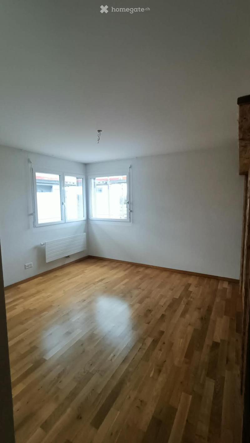 Empty room with wooden flooring, white walls, and two windows with white frames. A radiator is visible on one wall.