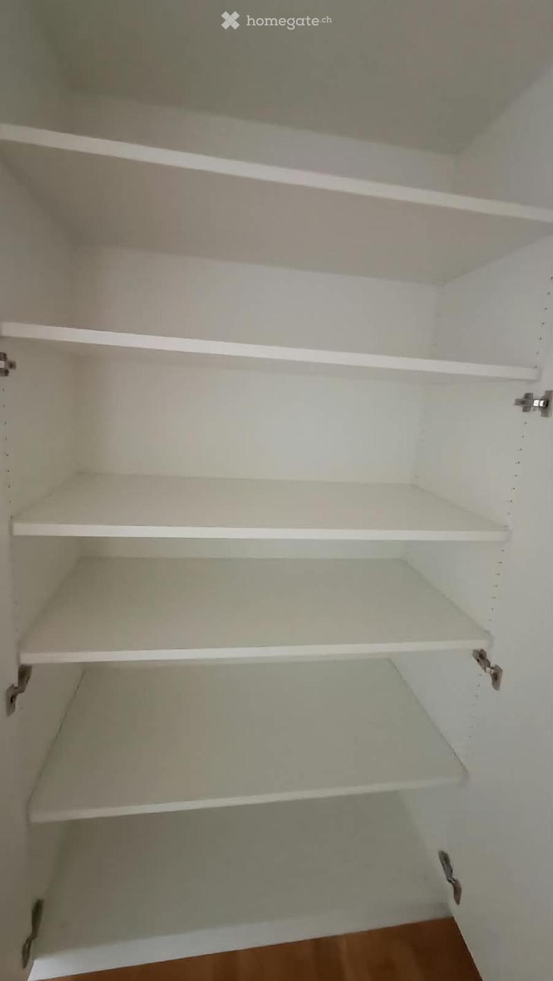 Empty white cabinet with multiple open shelves, no items inside, against a light-colored wall.