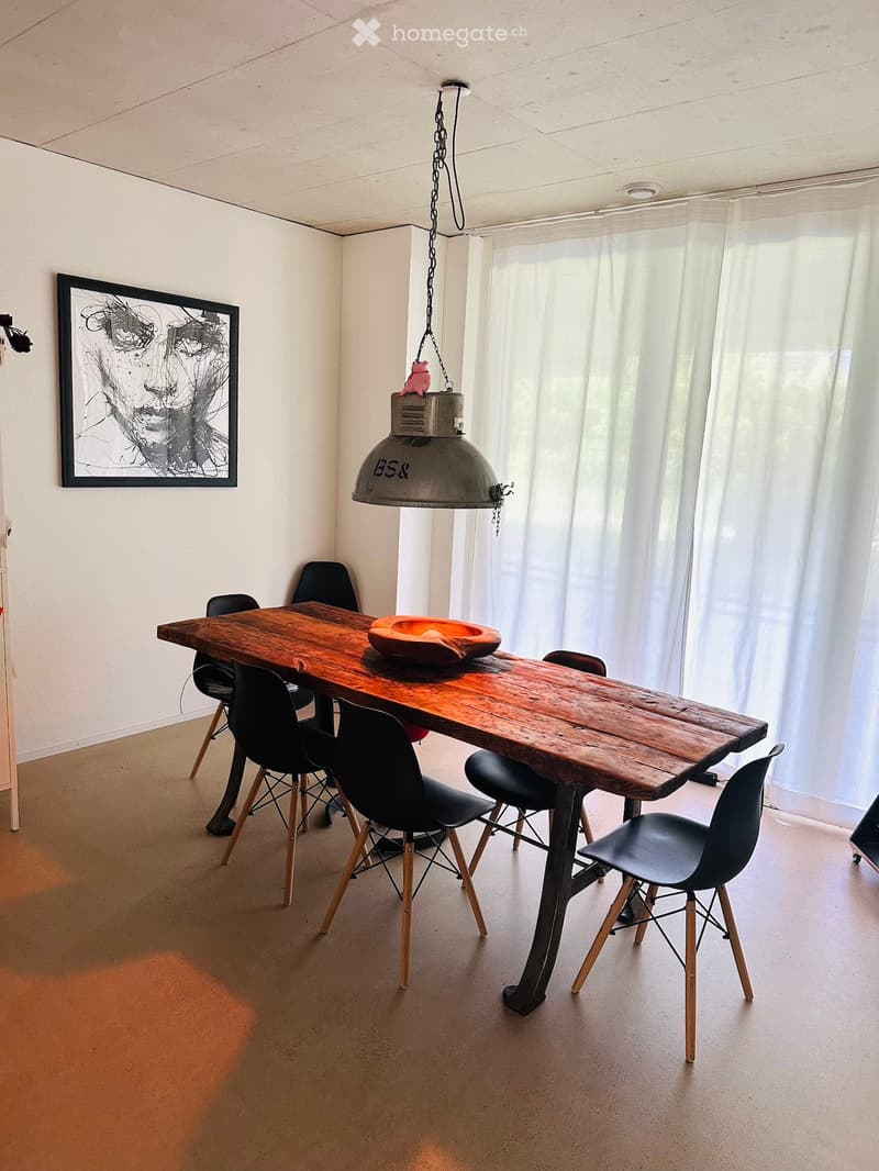 Dining area with a wooden table, black chairs, a bowl on the table, a large pendant light, and a picture frame on the wall.