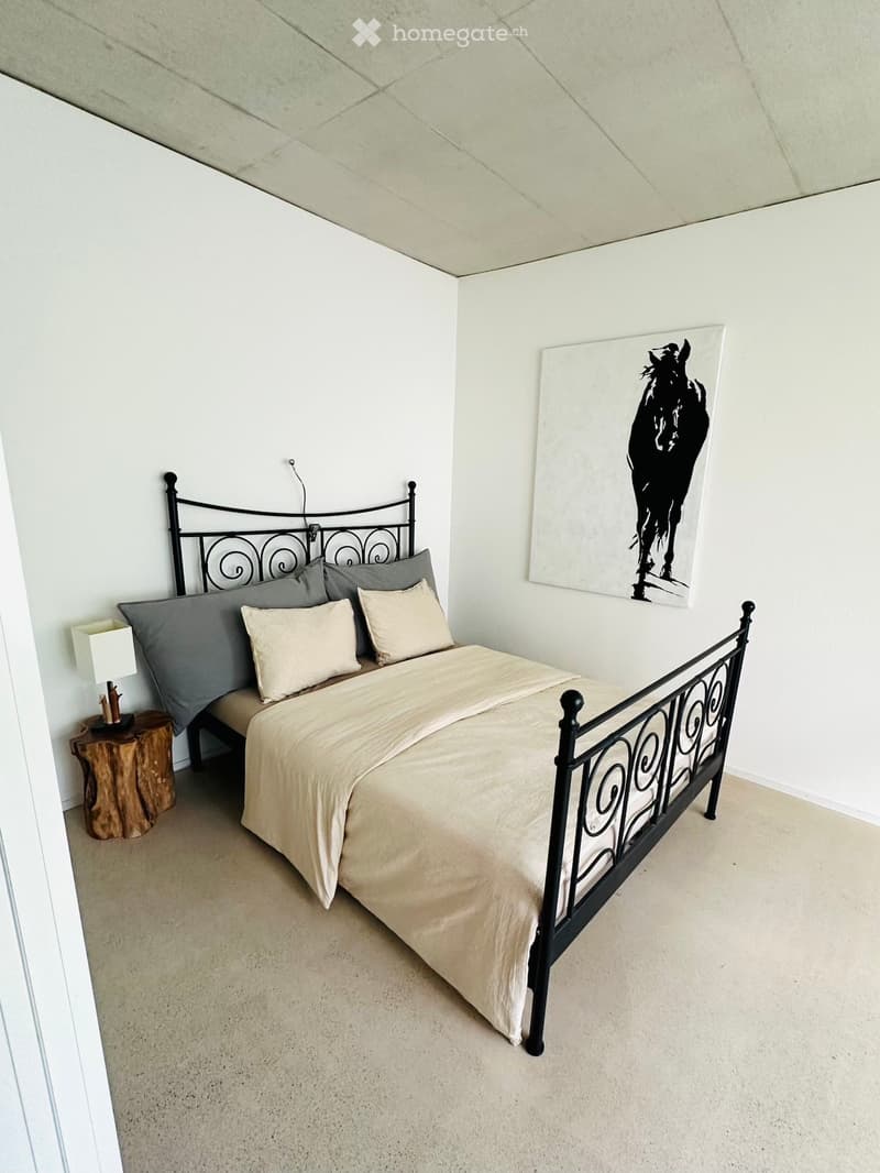 Bedroom with a metal-framed bed, beige bedding, nightstand with lamp, and a picture of a horse on the wall.