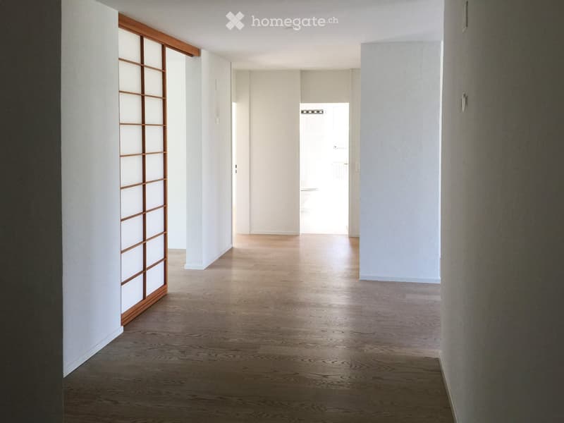 Empty hallway with wooden flooring, white walls, and a sliding door on the left side.