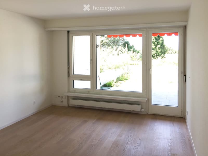 Empty room with wooden flooring, white walls, large windows, and a sliding glass door leading to an outdoor area.