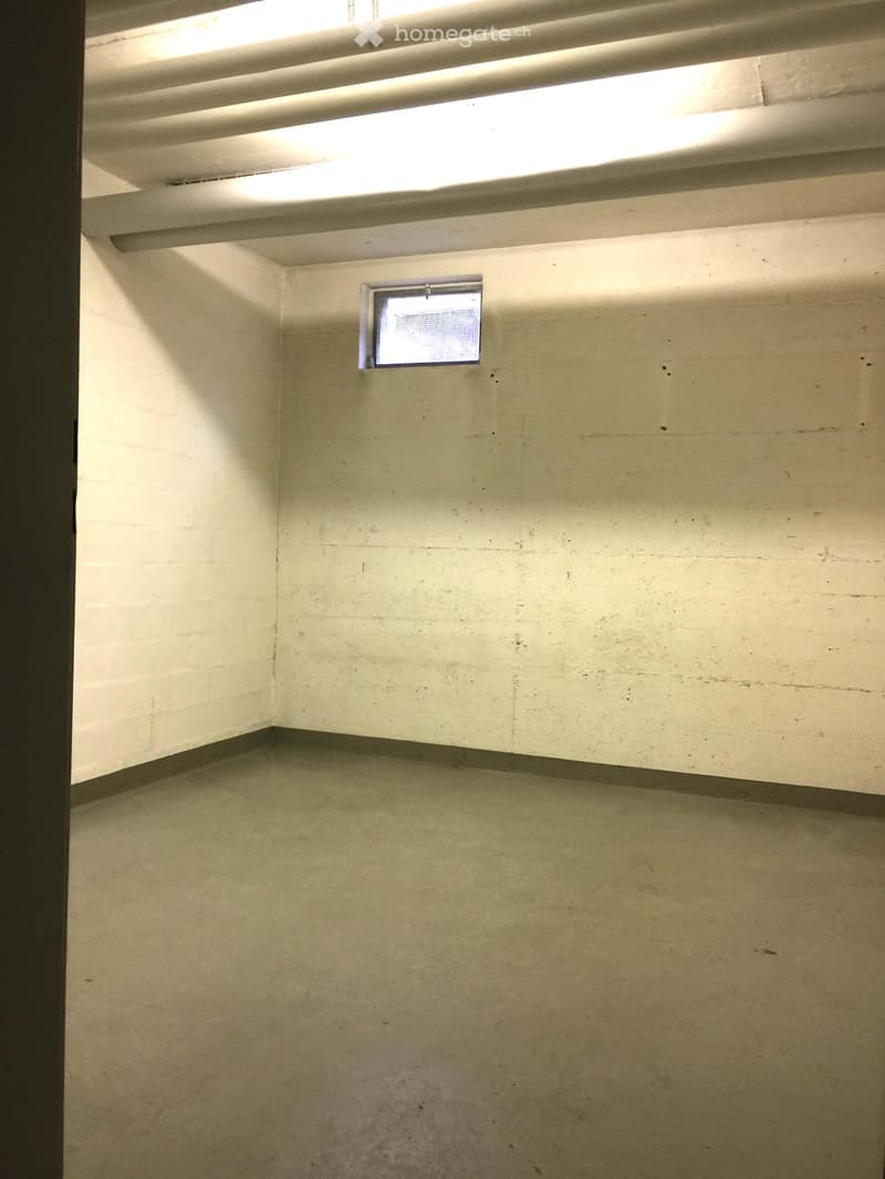 Empty room with bare walls and a concrete floor, featuring a small screen mounted on the wall and a fluorescent light fixture on the ceiling.