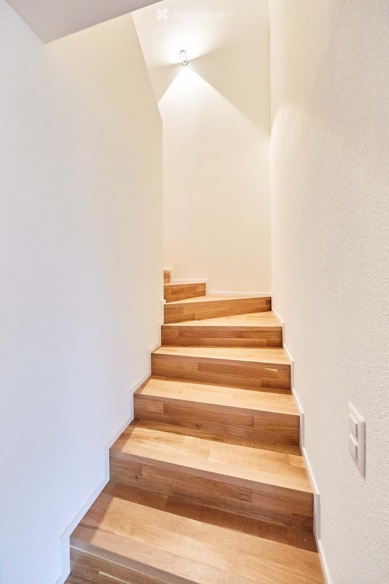 Modern staircase with wooden steps and white walls, illuminated by a small spotlight.