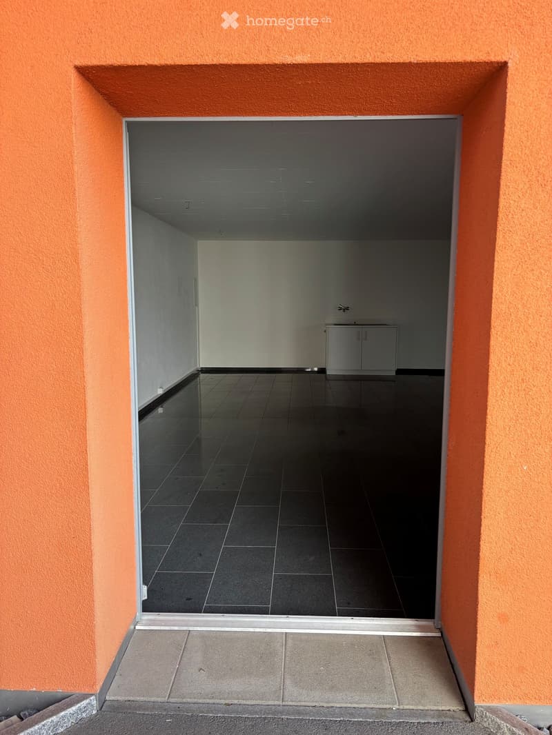 Empty room with dark tiled floor, white walls, and a small cabinet with a sink in the background.