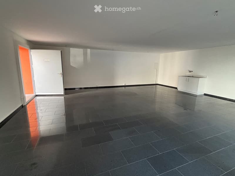 Empty room with white walls, dark tiled floor, and a small white cabinet with a sink in the corner.