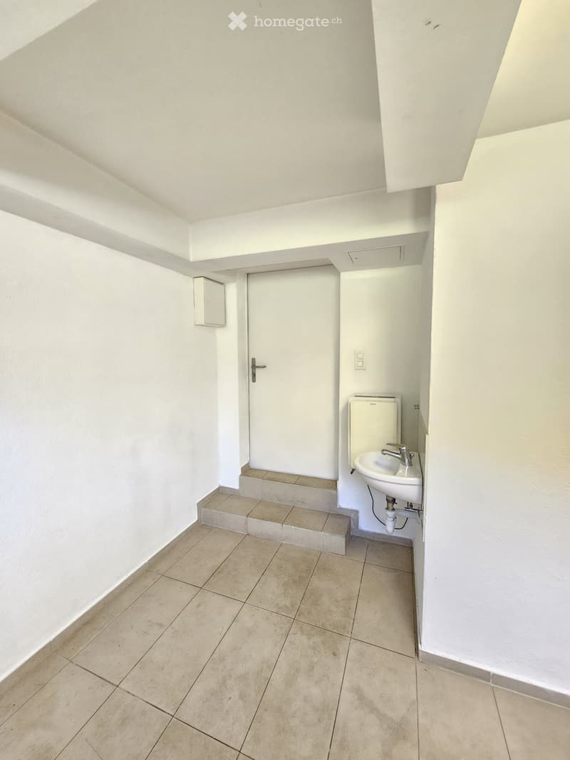 Empty room with tiled floor, white walls, a door, and a small sink area with a faucet.