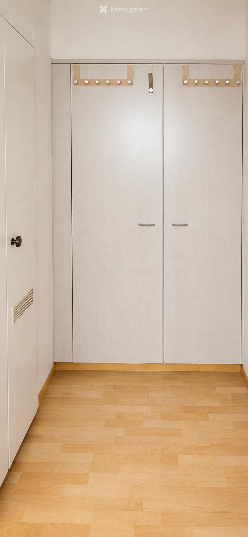 Empty room with light wooden flooring and white built-in wardrobes with silver handles.