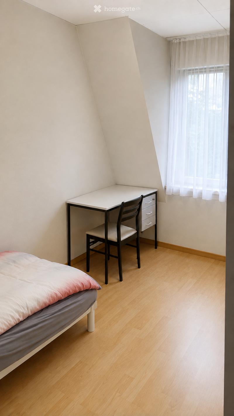 Cozy attic bedroom with wooden flooring, a bed with pink bedding, a desk with a chair, and a window with white curtains.