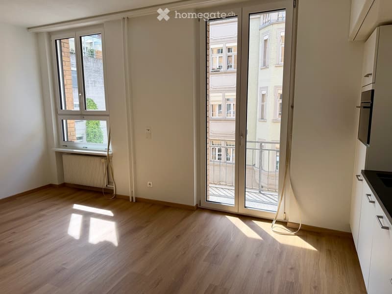 Empty room with wooden flooring, large windows, and a sliding glass door leading to a balcony. The walls are light-colored, and there is a radiator under one window.