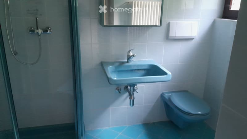 A small bathroom with light blue tiles, a sink with a modern faucet, a toilet, a mirror above the sink, and a glass-enclosed shower area.