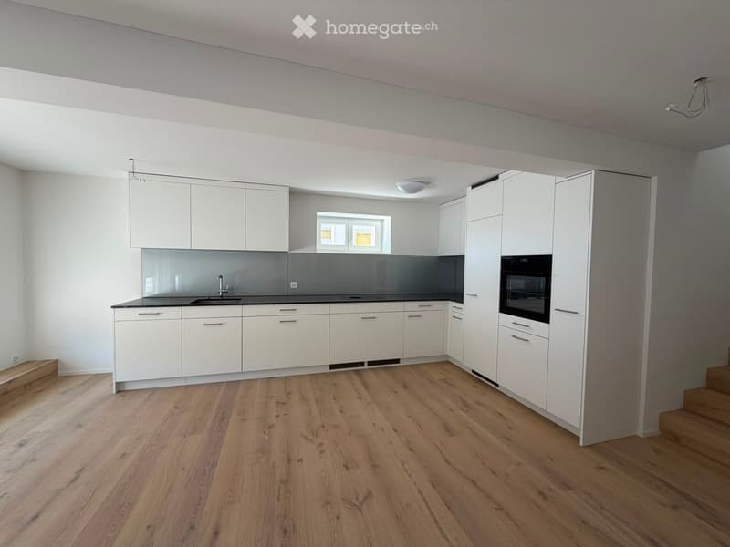 Empty kitchen with white cabinets, black countertops, and wooden flooring. No appliances or furniture are present.