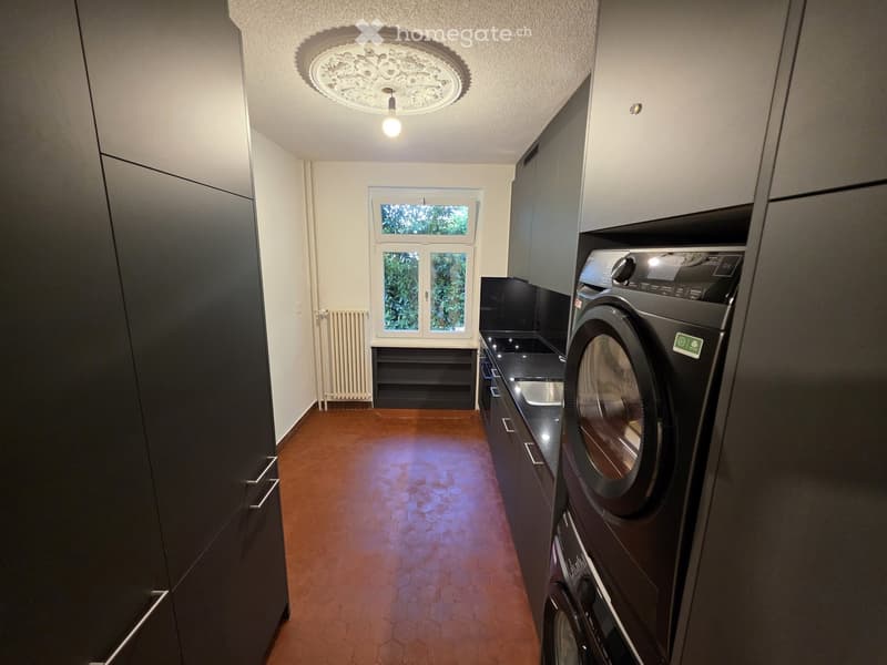 Modern hallway with dark cabinets, a washing machine, dryer, and a window with a view of greenery.