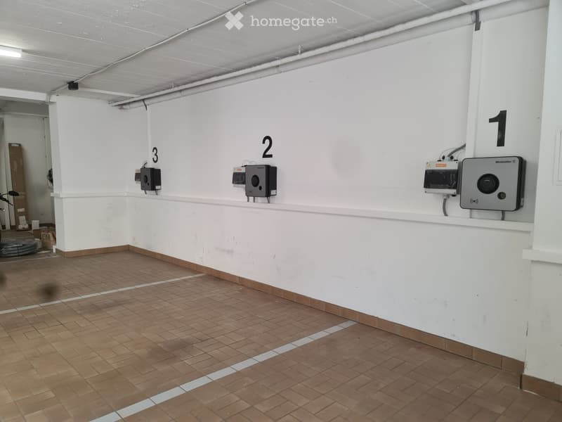 Empty room with white walls, tiled floor, and numbered charging stations for electric vehicles.