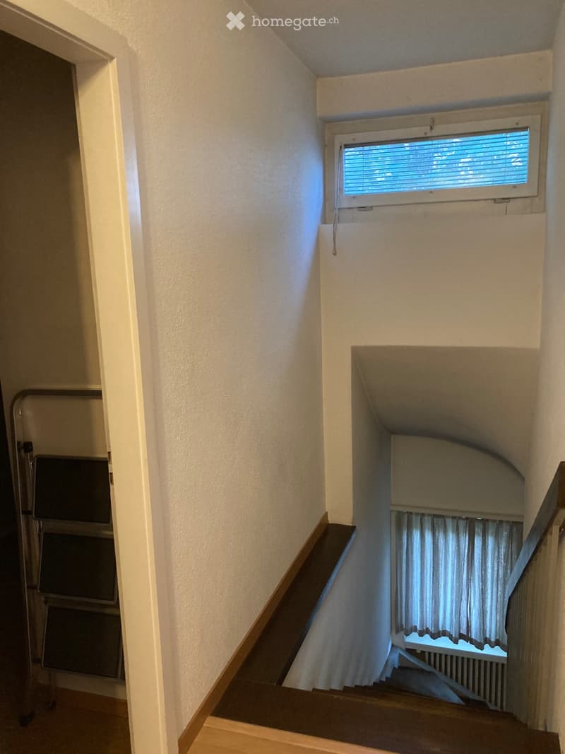 Staircase with wooden steps and handrail, white walls, windows with blinds, and a small landing area.