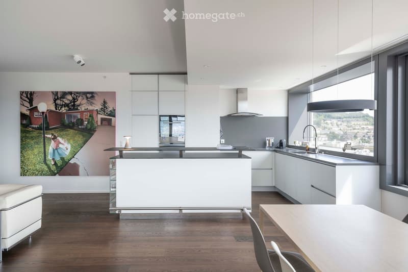 Modern kitchen with white cabinets, a central island, a dining area, and large windows offering a city view.