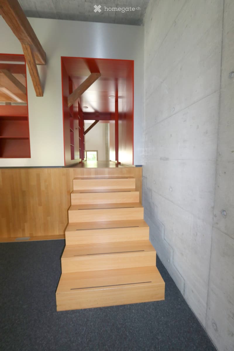 Modern wooden staircase with a sleek design, featuring a red accent wall and a concrete wall on the right side.