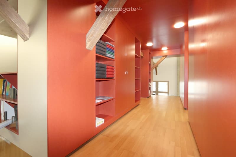 Modern hallway with red walls, wooden floor, built-in shelving units, and a staircase leading upwards.