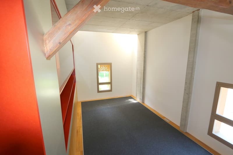 Empty hallway with white walls, wooden floor, and small windows allowing natural light.