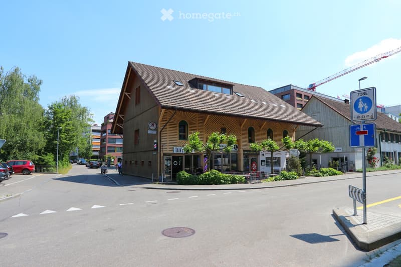 A multi-story building with a wooden facade and tiled roof, located on a street corner with a sign indicating a pedestrian zone.