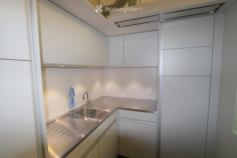 Modern kitchen with white cabinets, stainless steel sink, and countertop. Features built-in lighting and a sleek design.
