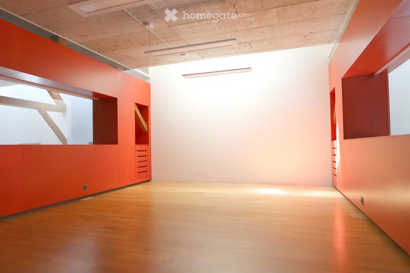 Bright, empty room with wooden flooring and red accent walls, featuring built-in storage units and large windows allowing natural light to fill the space.