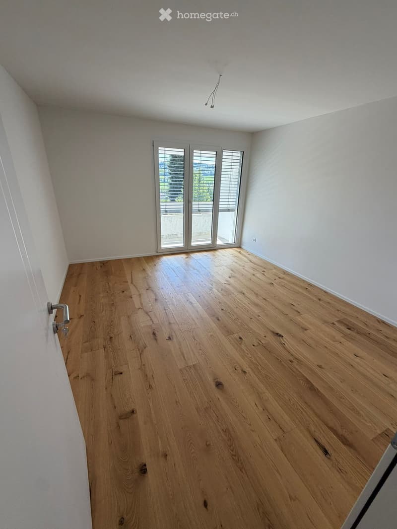 Empty room with light wooden flooring, white walls, and large sliding glass doors leading to a balcony.