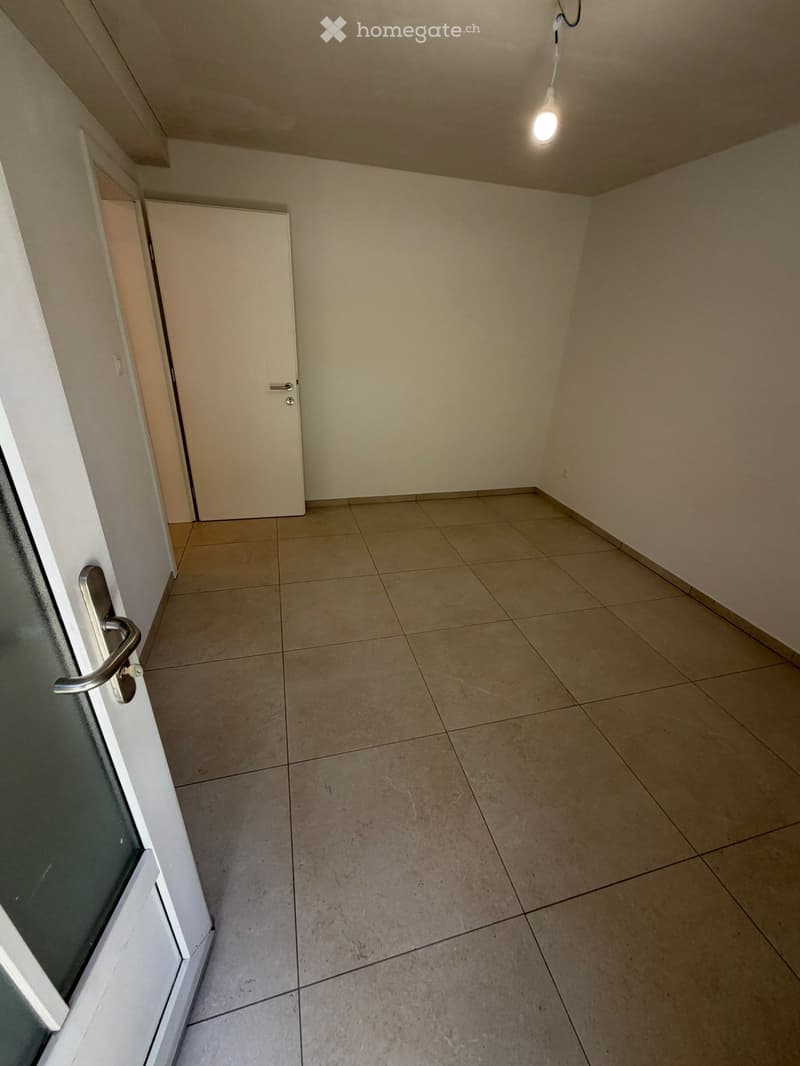Empty hallway with tiled floor, beige walls, and a closed door at the end.